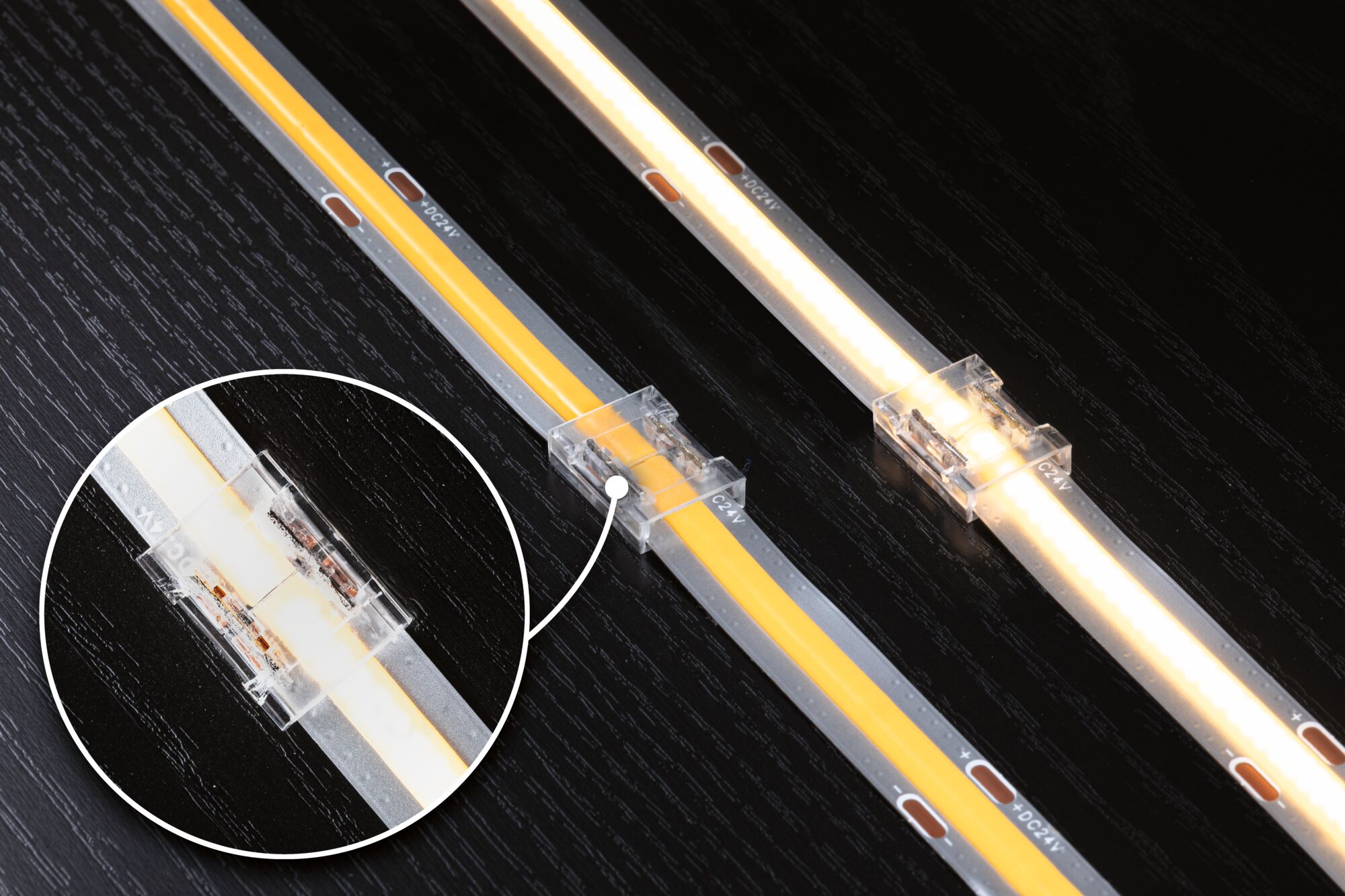 LED-Lichtstreifen mit transparentem Verbinder auf schwarzer Holzoberfläche, warmweißes Licht, 24V Anschluss