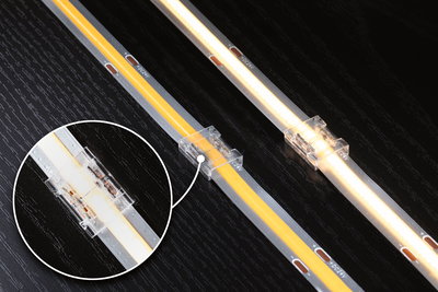 LED strip light with transparent connector on black wood surface, warm white light, 24V connection