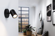Black metal LED wall light with adjustable spotlight head for modern indoor lighting solutions.