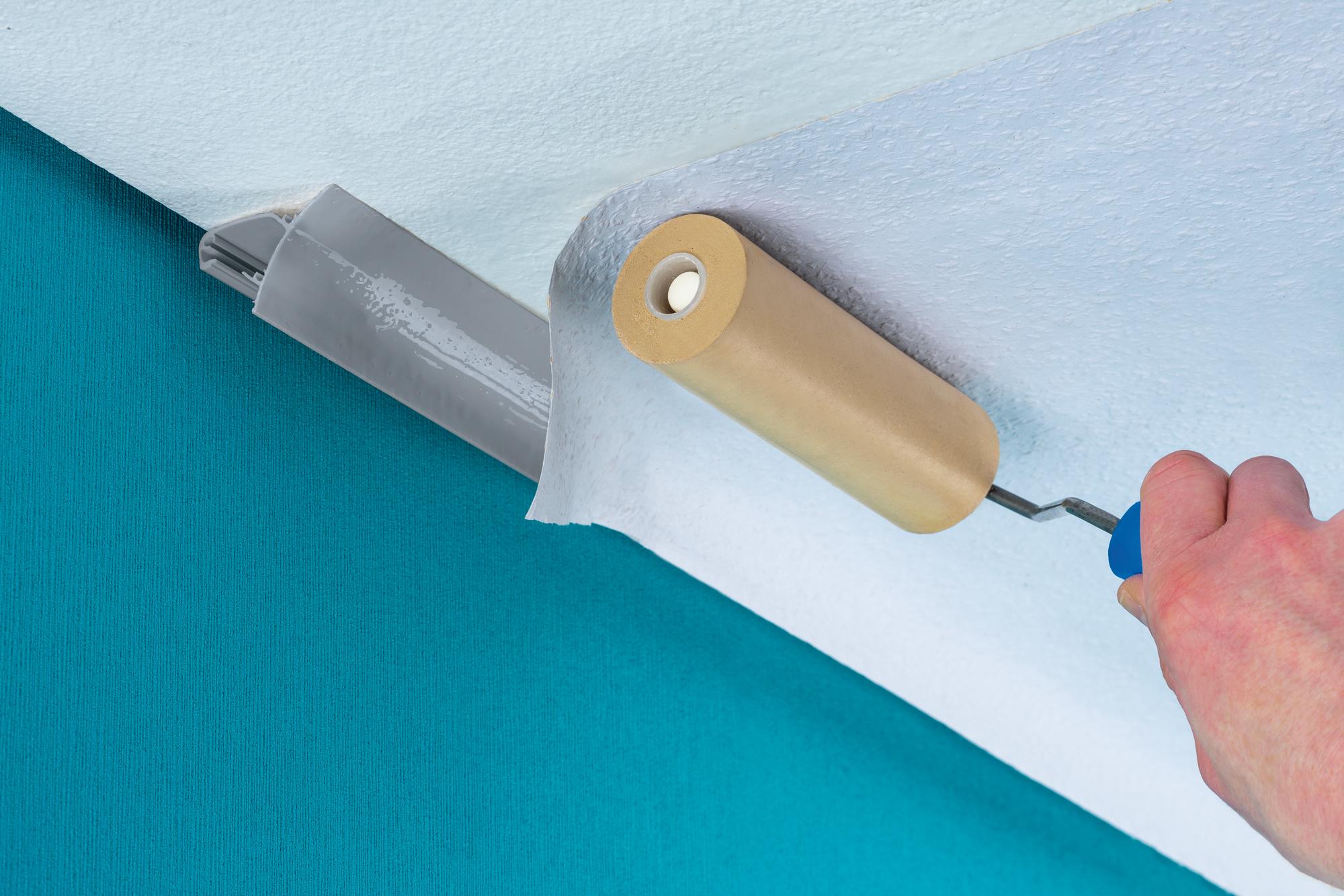 Hånd med blå malerrulle fjerner hvid tapet fra blå væg til renovering og vægdekoration