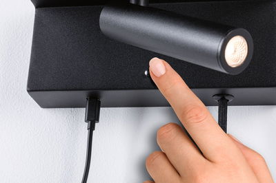 Schwarze LED-Wandleuchte aus Metall mit integriertem Schalter und USB-Ladeanschluss an weißer Wand