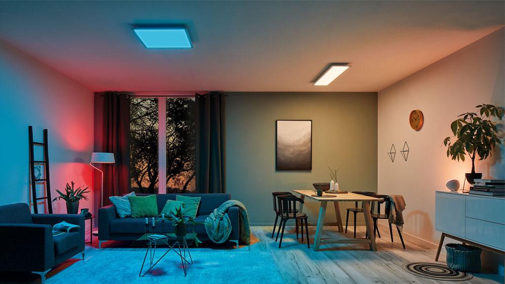 Modernes Wohnzimmer mit blauer und roter LED-Deckenbeleuchtung und gemütlicher Sitz- und Essbereich.