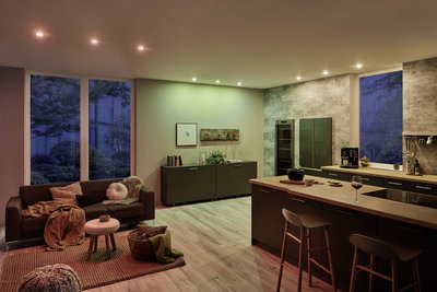 Wohnraum mit warmweißen und farbigen LED-Downlights, moderner Küche und gemütlicher Sitzecke mit Sofa.