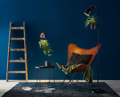 Gezellige leeshoek met bruine leren vlinderstoel, plantenlampen en blauw vloerkleed voor sfeerverlichting thuis.