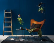 Lampes pour plantes modernes noires et cuivre éclairant des plantes vertes devant un mur bleu foncé dans un salon.