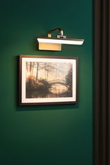 Wandlampe aus gebürstetem Metall mit warmweißem LED-Licht über gerahmtem Naturbild an grüner Wand