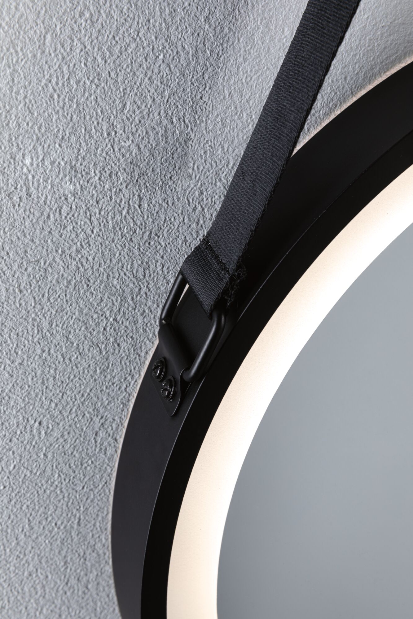 Round black LED mirror with integrated light and black hanging strap on textured wall