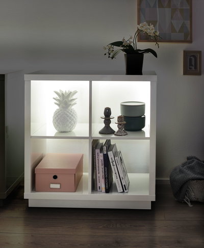White illuminated shelf with ceramic pineapple, candle holders, box and books in modern living room