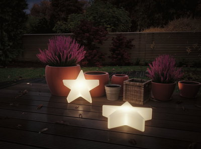 Twee witte LED-sterlampen op houten terras met terracotta potten en paarse planten in tuin bij schemer.