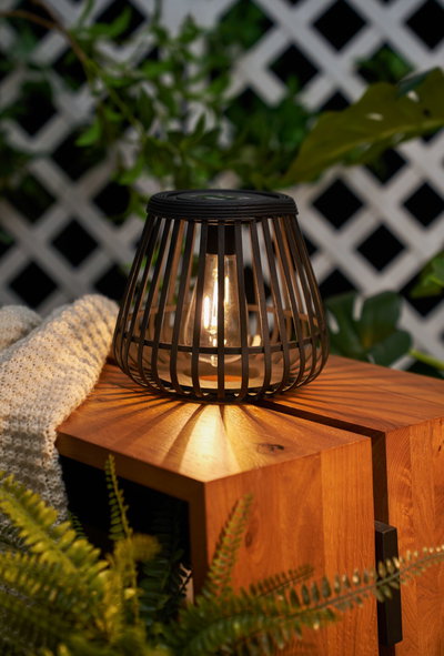 Black metal table lamp with open grid design on wooden surface, ambient LED lighting for garden use.