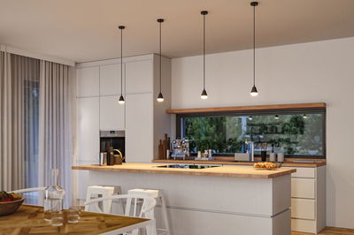 Moderne Küche mit vier schwarzen Pendelleuchten aus Metall und Holzarbeitsplatte, Tageslichtfenster.