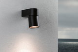 Moderner schwarzer Aluminium-Wandstrahler mit warmweißem Licht an grauer Außenwand mit Meerblick