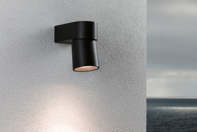 Moderner schwarzer Aluminium-Wandstrahler mit warmweißem Licht an grauer Außenwand mit Meerblick