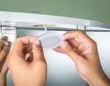 Hands installing white plastic LED under-cabinet light on furniture with green background