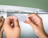 Hands installing white plastic LED under-cabinet light on furniture with green background