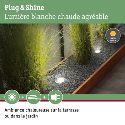 Spot LED encastré au sol avec lumière blanc chaud dans un lit de gravier près des herbes décoratives