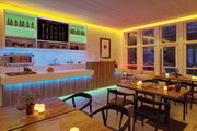 Modern bar interior with warm and cool LED strip lighting, wooden counter and white tiled wall