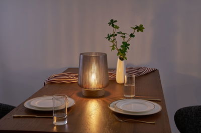 Lampe de table en verre à motif avec base en bois sur table en bois dressée avec vaisselle et vase.