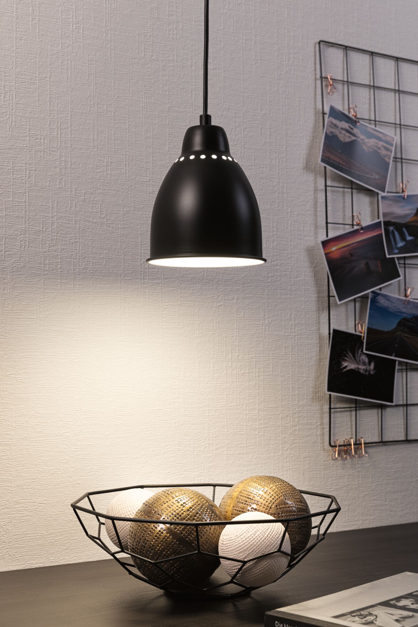 Zwarte metalen hanglamp met ronde lichtgaten en decoratieve draadmand met ballen op tafel