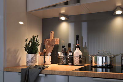 Modern kitchen countertop with wood, stainless steel pot, herb pot, and spice containers under LED wall lights.