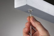 Hand hält silbernes Stahlseil an gebürstetem Aluminiumprofil für moderne LED-Hängeleuchte.