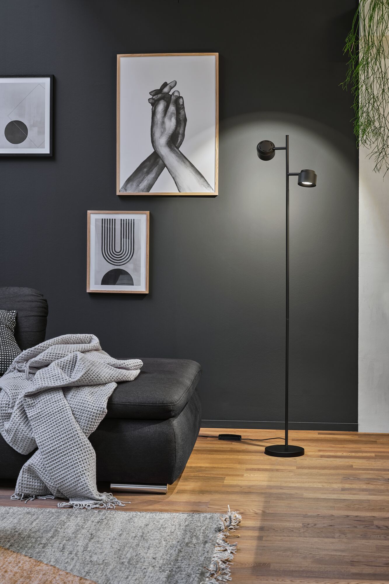 Black floor lamp with two adjustable spotlights in modern living room with dark wall and wooden floor