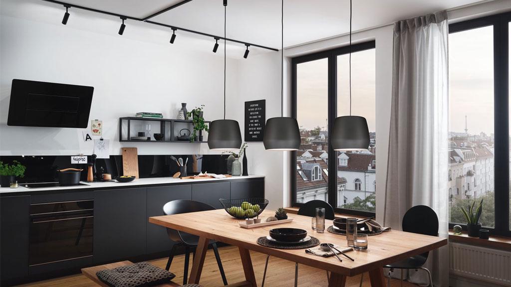 Moderne Küche mit schwarzer Küchenzeile, Holz-Esstisch und drei schwarzen Pendelleuchten für Küchenbeleuchtung.