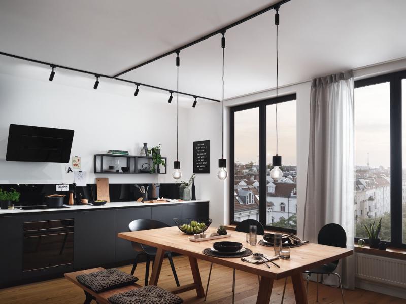 Modern kitchen with black URail track lighting and wooden dining table with black chairs in bright room.