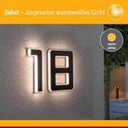 Solarhausnummer aus schwarzem Material mit warmweißem LED-Licht an grauer Wand