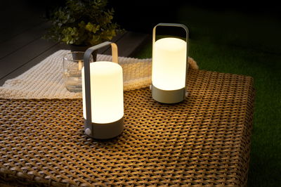 Twee draagbare grijze LED-tafellampen met warm wit licht op gevlochten tuintafel.