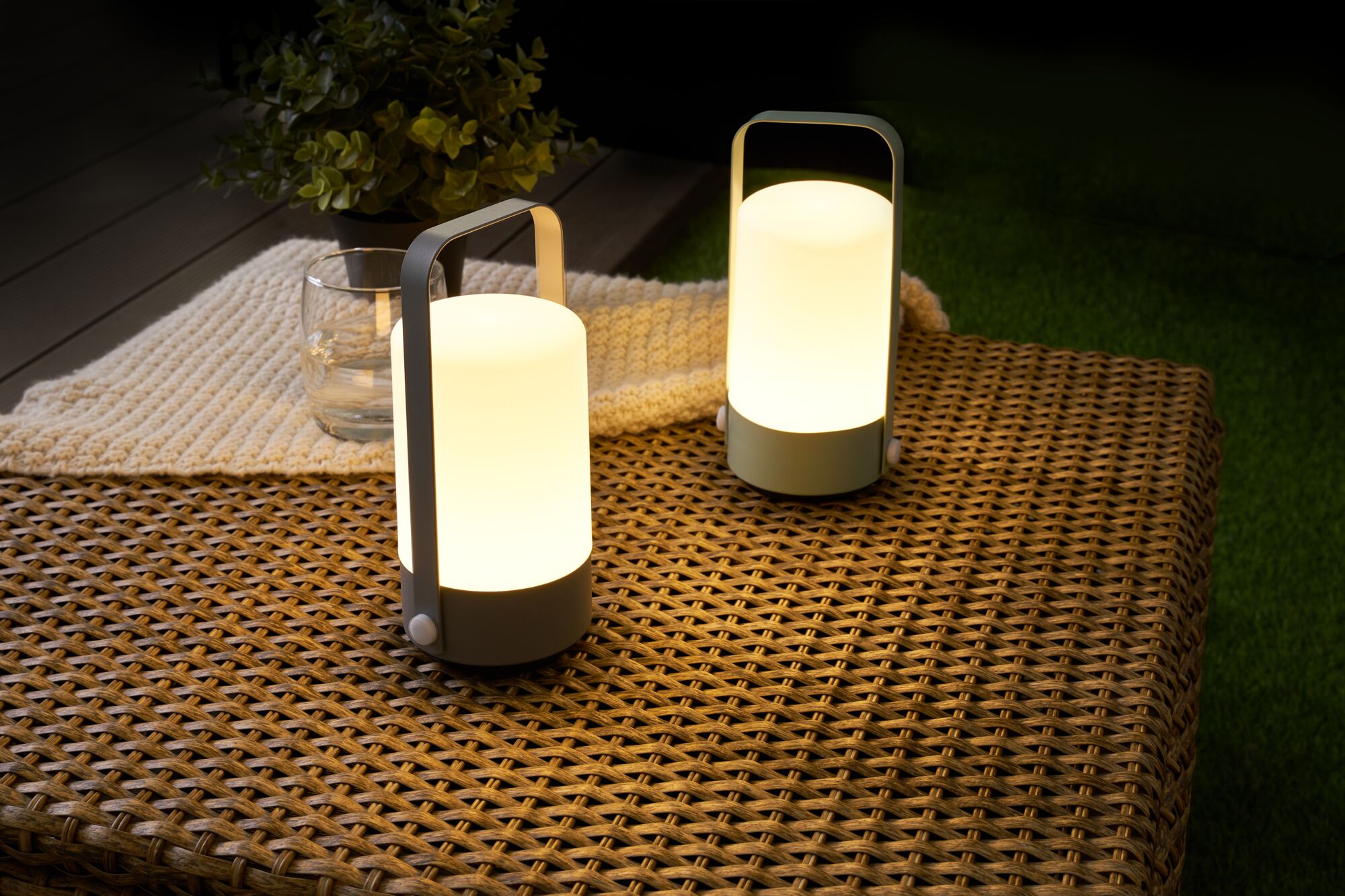 Two portable grey LED table lamps with warm white light on woven outdoor table for garden lighting