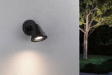 Black metal outdoor wall light with warm white LED on white wall in garden setting