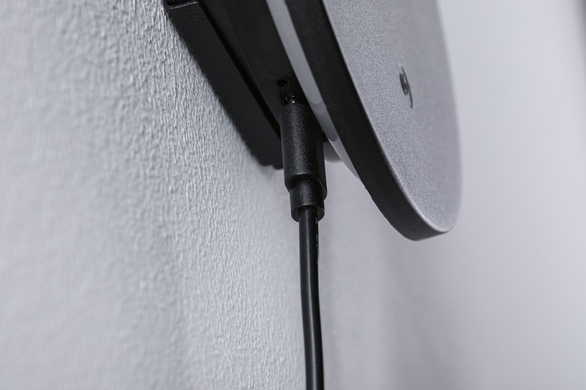 Close-up of black cable connection on grey plastic wall mount with textured surface