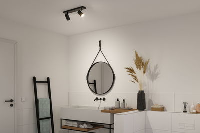 Salle de bain moderne avec plafonnier noir, miroir rond et lavabo blanc avec étagère en bois