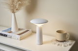 Modern white LED table lamp with conical base on light table next to cup and vase