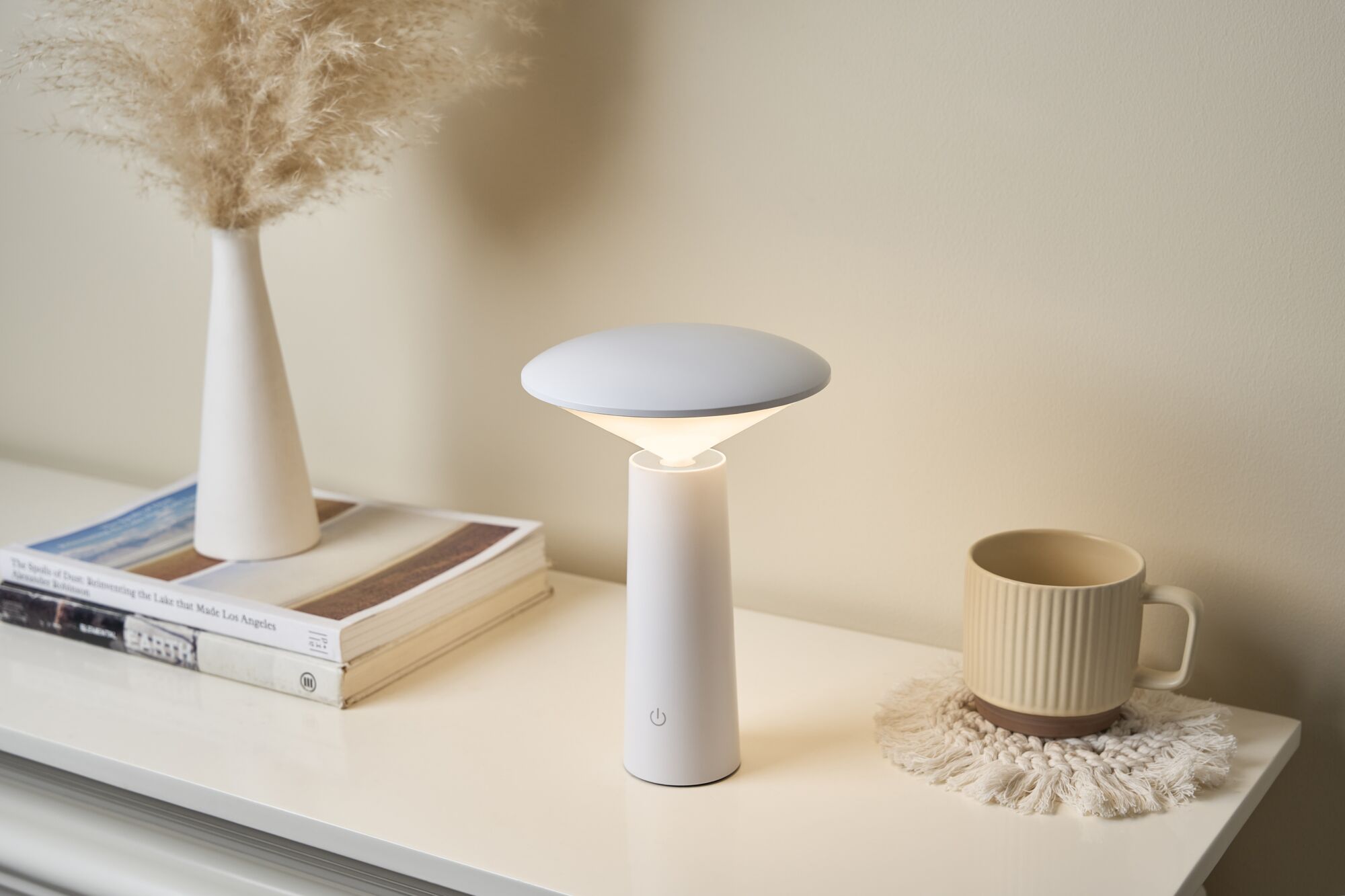 Modern white LED table lamp with conical base on light table next to cup and vase