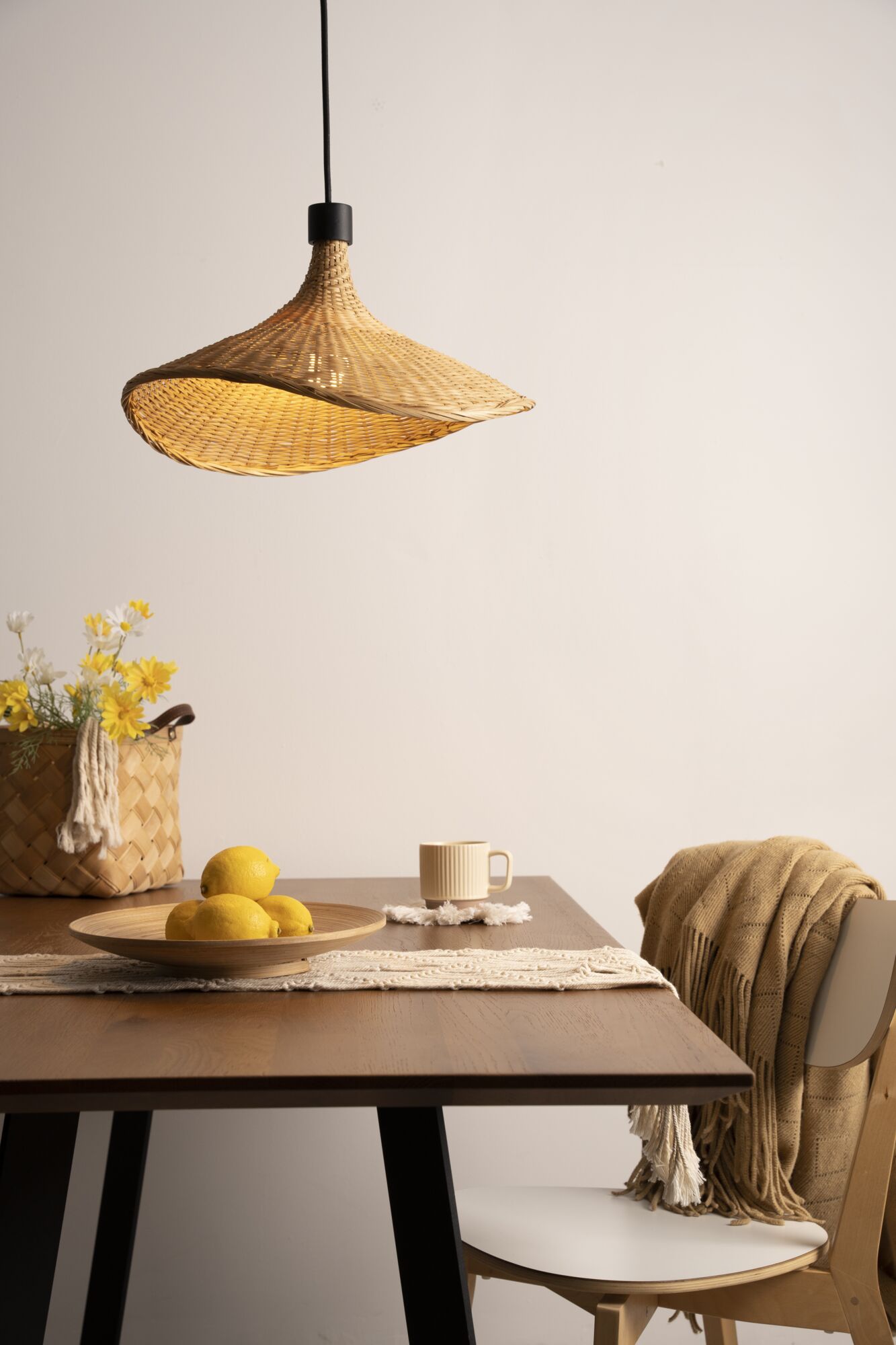 Lampa wisząca z plecionego naturalnego materiału w beżu nad drewnianym stołem z cytrynami i kubkiem