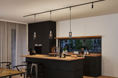 Modern kitchen with black wood finish, wooden countertop, pendant lights, and bar stools in dining area