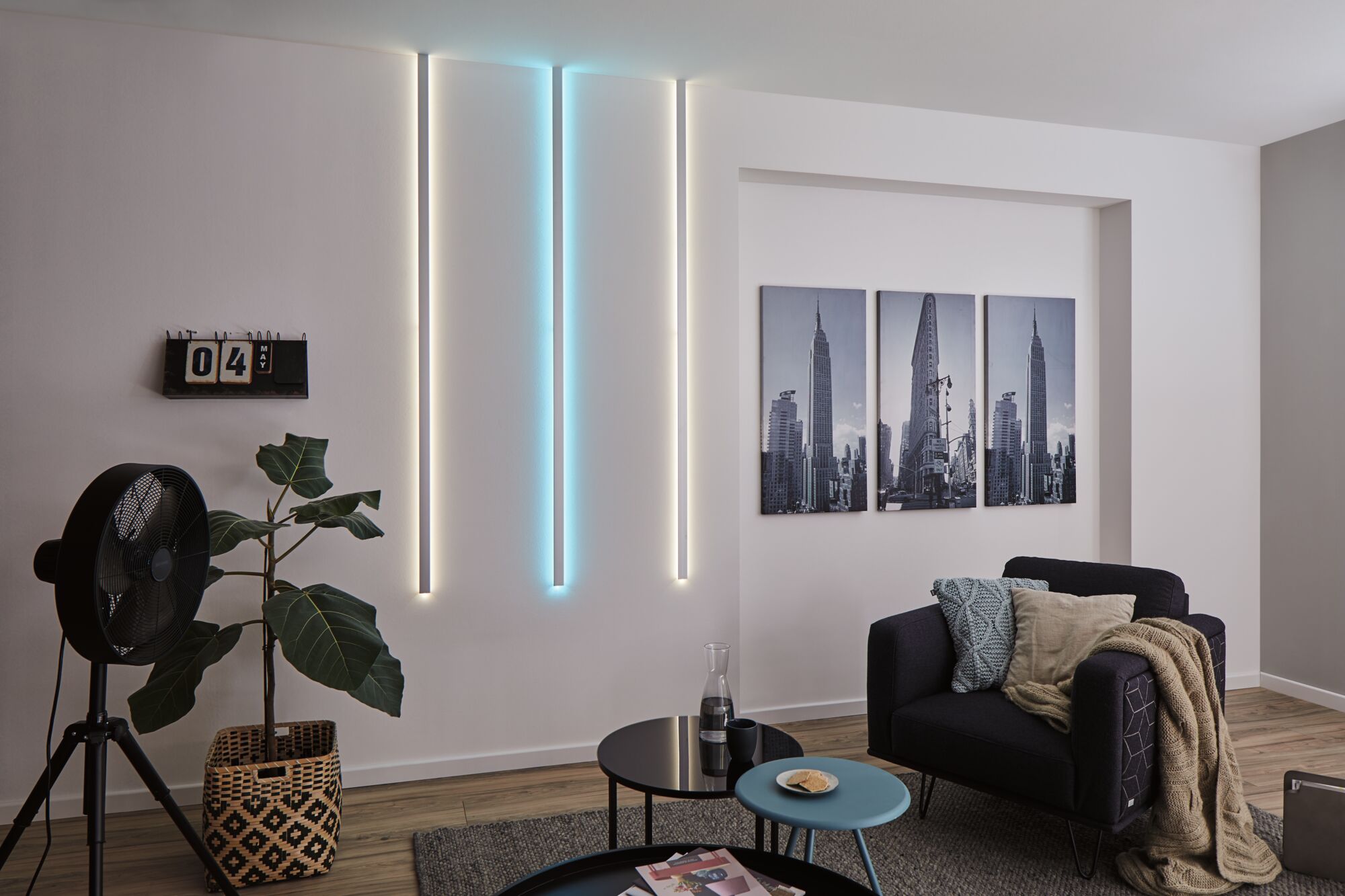 Modernes Wohnzimmer mit LED-Wandbeleuchtung in Weiß und Blau, schwarzem Sessel und Stadtbildern.