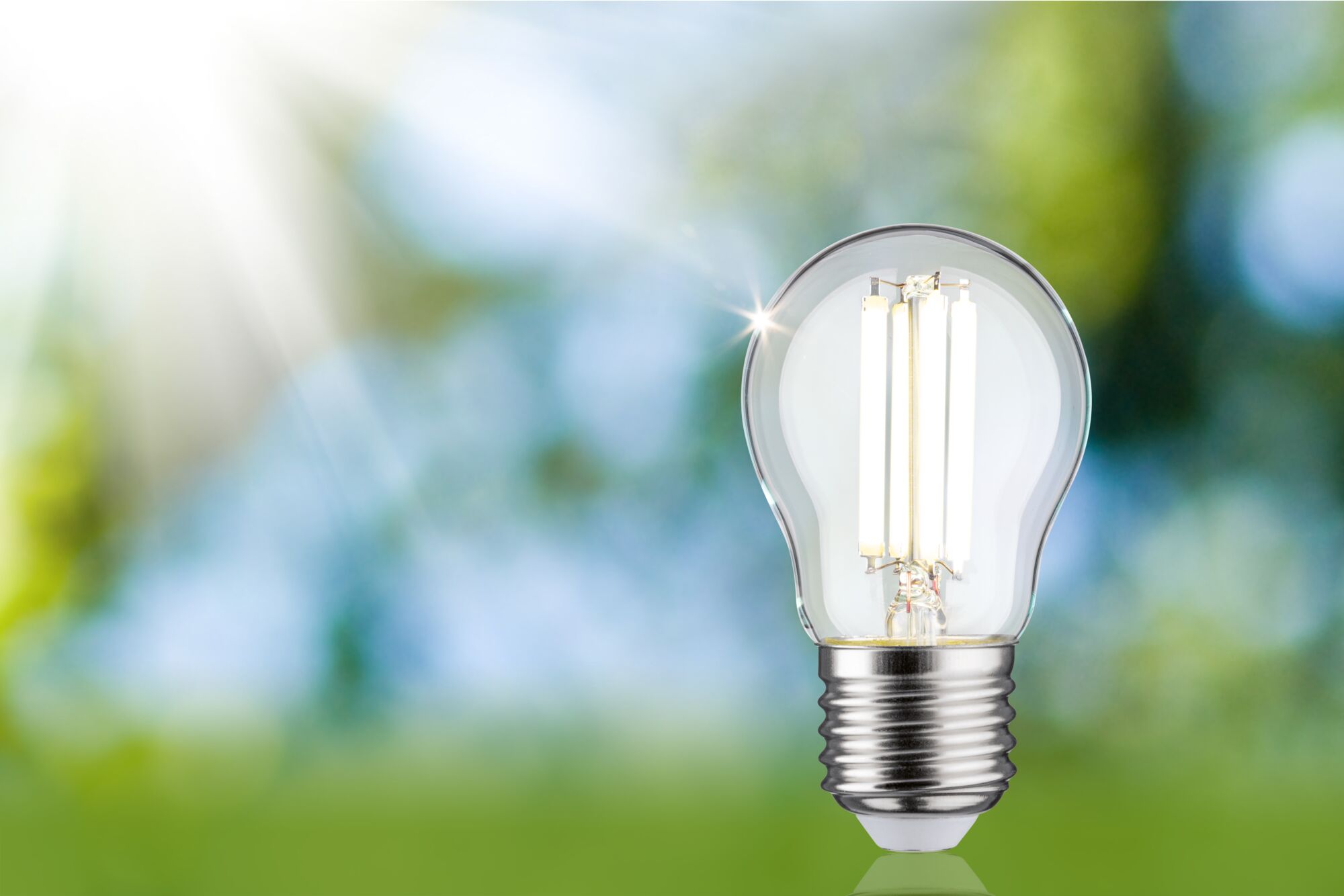 LED light bulb with clear glass and silver base against green-blue background for energy-saving lighting