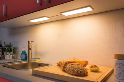 Küchenarbeitsplatte mit Edelstahlspüle, Holzschneidebrett, Sesam-Brot und Muffin unter warmweißer LED-Unterbauleuchte