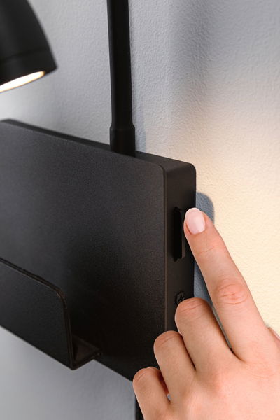 Black metal wall lamp with switch operated by hand, modern LED wall light for living spaces.