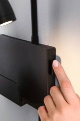 Black metal wall lamp with switch operated by hand, modern LED wall light for living spaces.