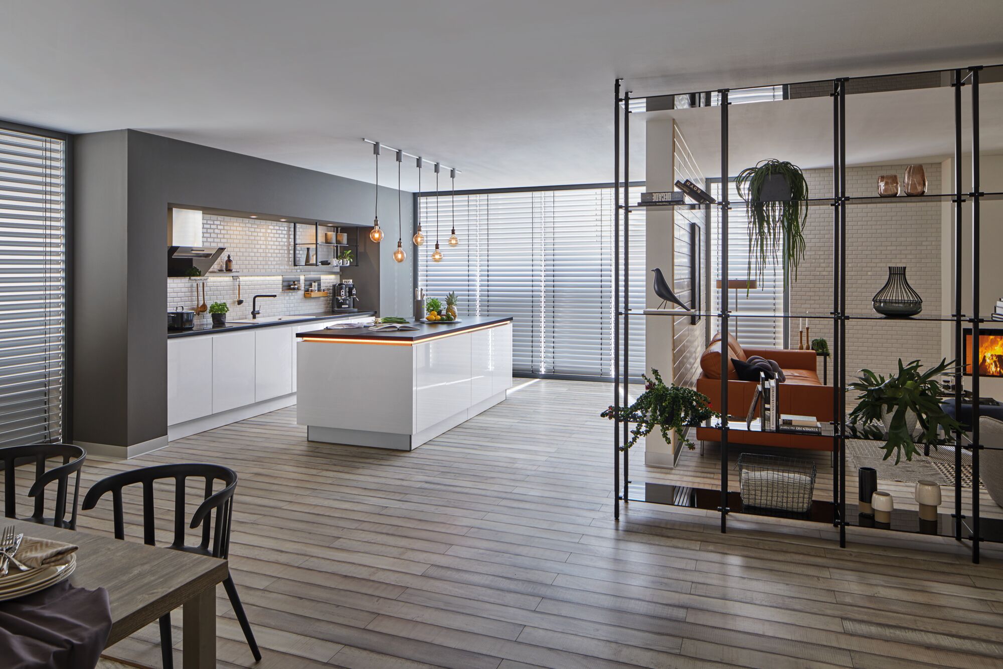 Moderne open keuken met wit eiland, houten vloer en zwarte hanglampen in woonkamer.