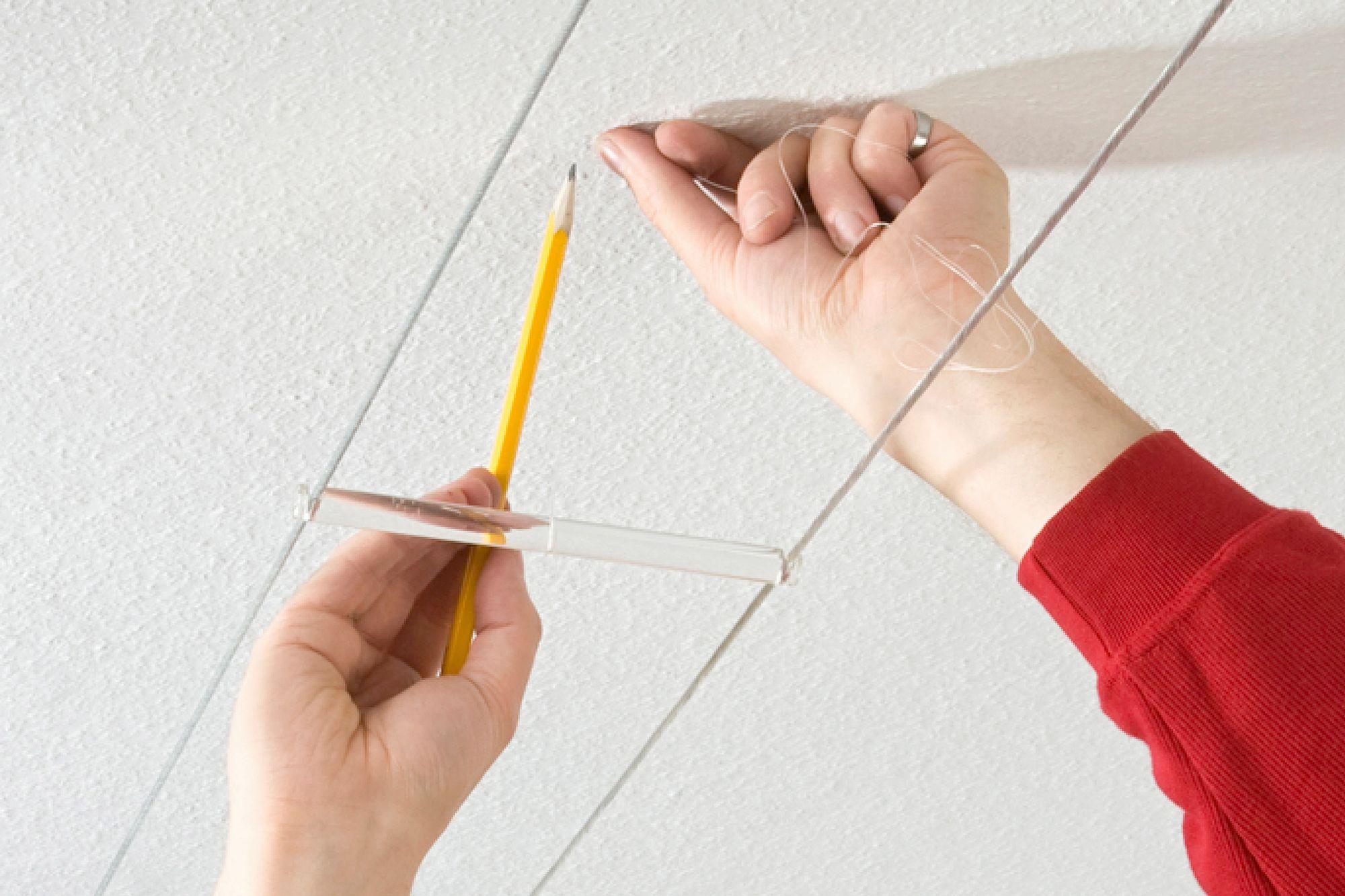 Hånd holder blyant og klar afstandsholder mod hvidt loft til LED-kabellys installation