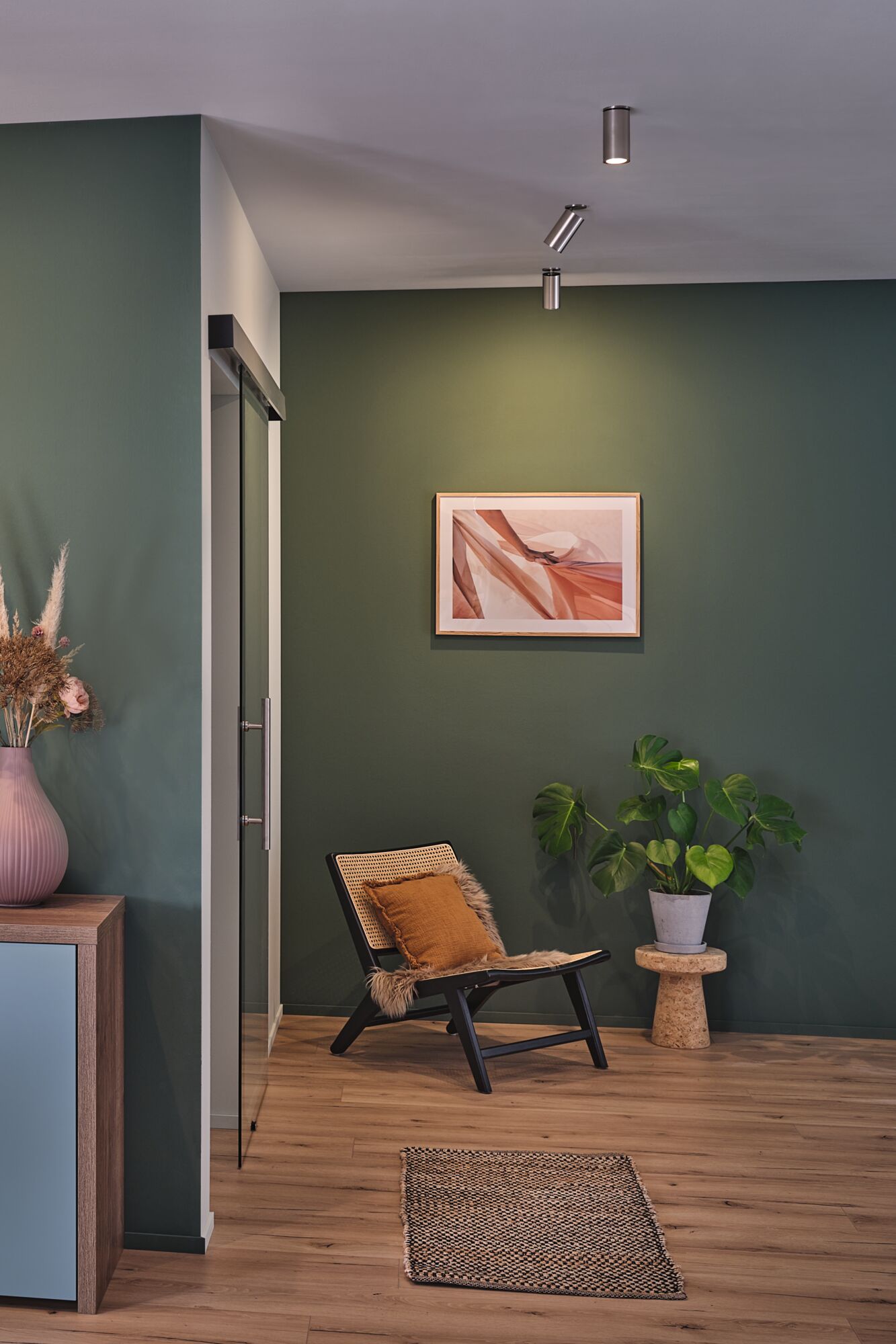 Modern living area with green painted wall, wooden chair with cushion and plant on cork stool