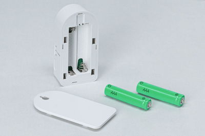 White battery compartment with cover and two green AAA batteries on grey background