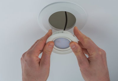 Mains installant un spot LED encastré blanc avec cadre en plastique au plafond, éclairage économique