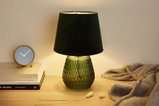 Grüne Glas-Tischlampe mit schwarzem Stoffschirm auf Holzfläche neben Uhr und Decke