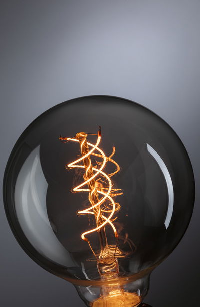 Close-up of a light bulb with spiral LED filament emitting warm light for decorative lighting